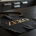 Delantales personalizados: delantal negro mate con detalle dorado sobre mesa de trabajo profesional