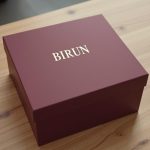 packaging para campañas estacionales: estuche rígido burdeos sobre mesa de roble claro visto desde arriba