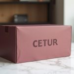 Packaging para envío de regalos corporativos: caja de envío de cartón ondulado burdeos sobre mesa de mármol blanco