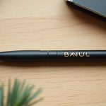 regalos de Navidad para clientes: bolígrafo negro mate con rotulación dorada sobre mesa de roble claro