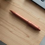 Tienda de merchandising para alumni: bolígrafo de aluminio terracota con grabado láser sobre mesa de roble
